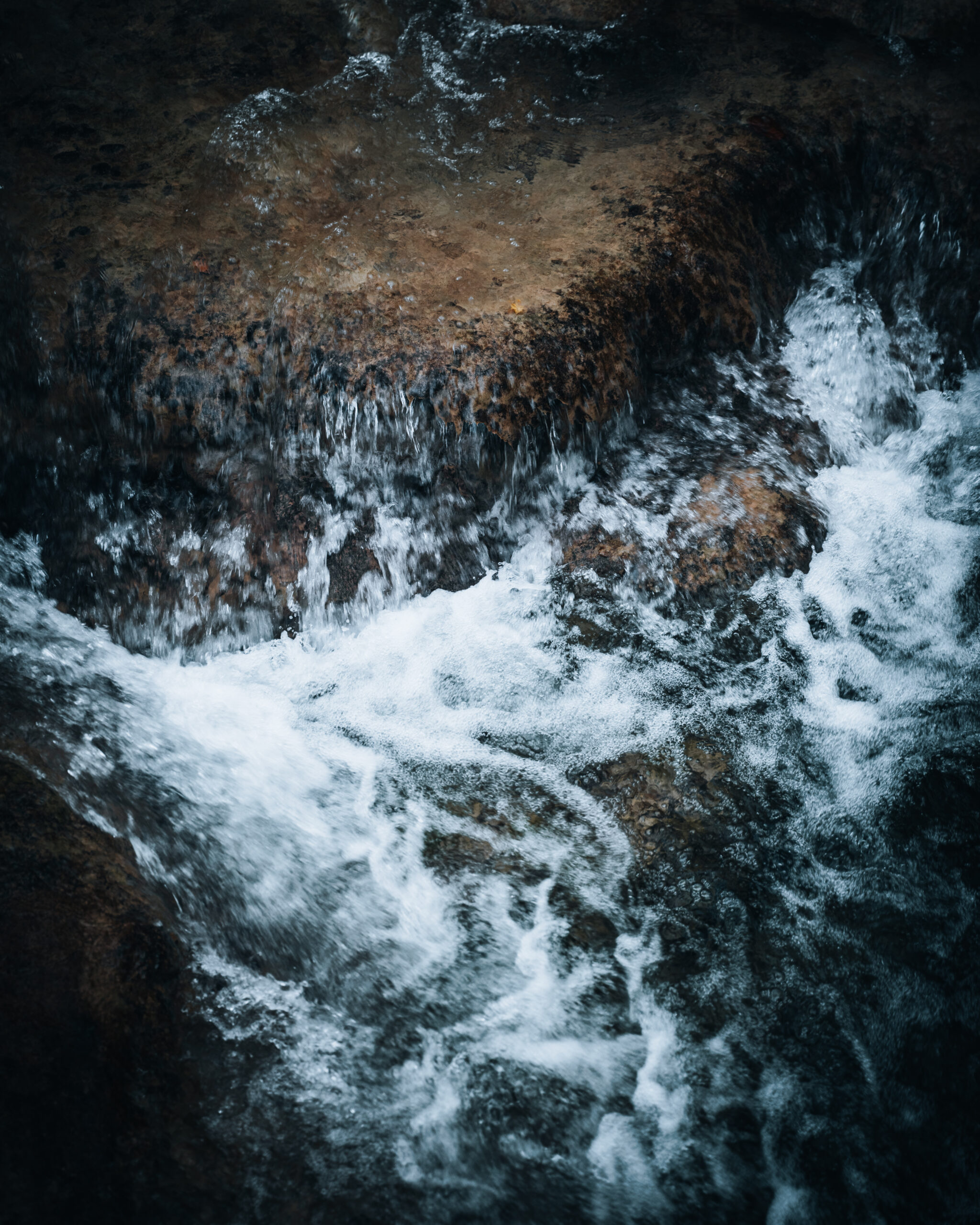 A fragment of flowing water, pulsing like a living vein across weathered stone, suspended between calm and force.